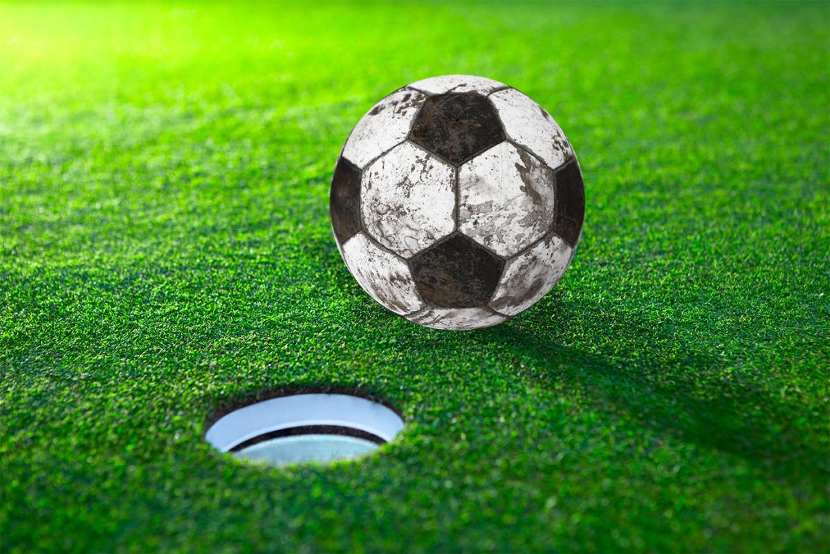 Balón de fútbol desgastado frente a hoyo de footgolf